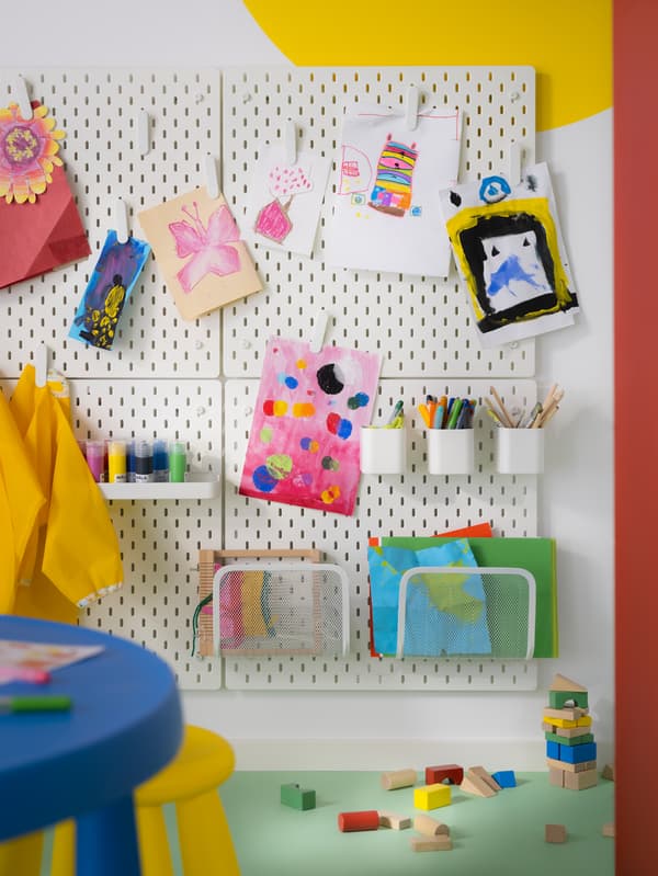Children’s artwork hang on four SKÅDIS pegboards. A SKÅDIS shelf, containers, and magazine holders keep art supplies tidy.