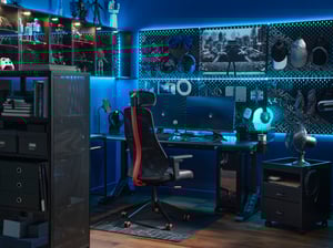 Gamerska soba, osvetljena z modro svetlobo, opremljena z dvema monitorjema, gaming stolom, pisalno mizo, omaricami, perforiranimi ploščami in vrsto gamerskih pripomočkov.