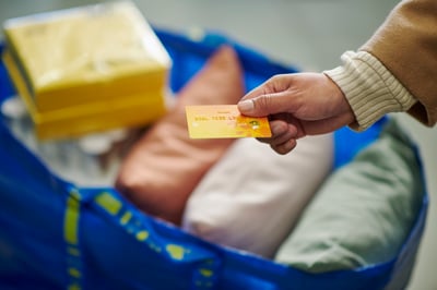 Kupac drži platnu karticu u ruci iznad IKEA vrećice s proizvodima
