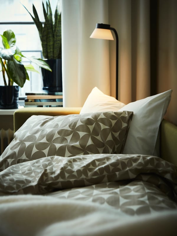 Part of a yellow-green SKÖNABÄCK 2-seat sofa-bed, used as a bed, with grey-beige/off-white ÄNGSNEJLIKA bed linen.
