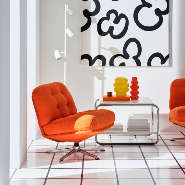 Two orange DYLINGE swivel armchairs are placed next to a coffee table with one yellow and one orange KÄLLARHALS vase on it.