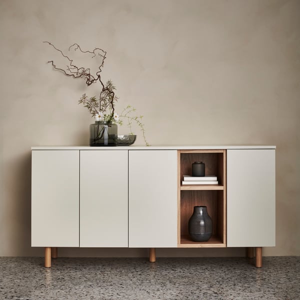 A LÅDMAKARE cabinet in grey-beige against a wall. A glass vase with flowers on top and a ceramic vase in the open section.