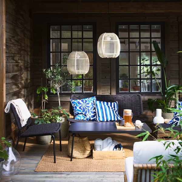 A cozy terrace with black TEGELÖN lounge furniture, blue and white pillows, and decorative SOLVINDEN lighting.