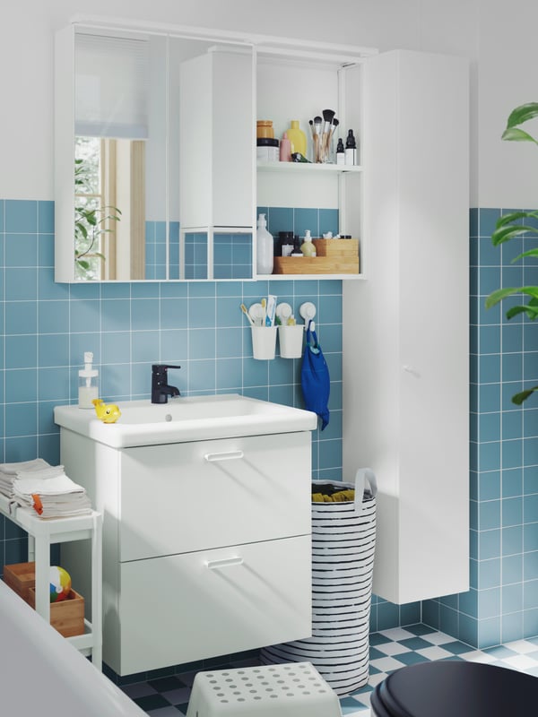 A blue-tiled bathroom with a bathtub has a white ENHET wash-stand, a mirror cabinet, a high cabinet and a VESKEN trolley.